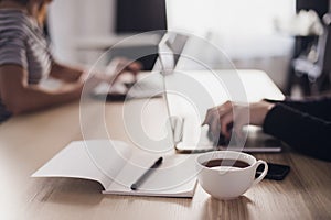 Close up picture of two businesswomen using tablet computer and laptop. Notebook with pen and cup of coffee in the