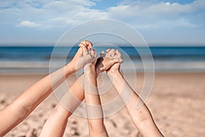 Close up picture of two little girls` hands holding together laying on the sandy ocean beach.