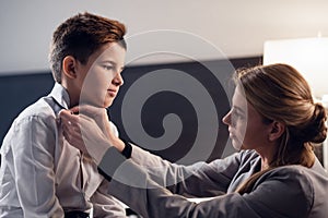 A close up picture of a woman fixing a young boy`s tie