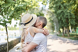 Close-up picture of young couple in love, hugging in park in summer, kissing. Pretty blond girl in stripy overall and straw hat on