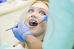 Close-up picture of young woman sitting in the dentist`s chair with opened mouth at dentist`s office while having