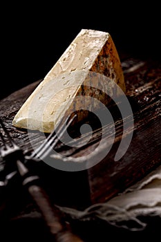 Close-up of a piece of cheddar cheese. Aged cheese made from farm milk, an old English recipe. A piece of cheese on a dark wooden