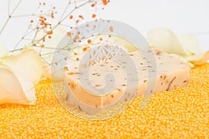 Close-up, a piece of handmade soap on scattered orange bath salts in the form of small balls