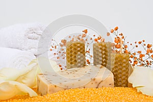 Close-up, a piece of handmade soap on scattered orange bath salts in the form of small balls, surrounded by white rose petals,