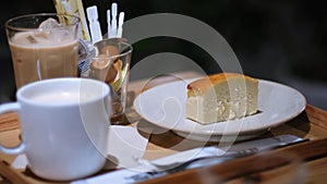 Close up piece of sweet homemade cheesecake on white plate with coffee and milk on wooden table