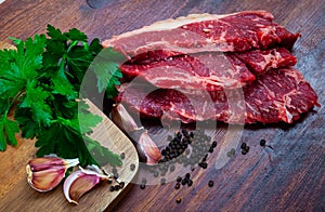 close up of pieces of marbled beef served with parley on wooden table