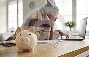 Close up of piggy bank on table with senior retired man using laptop computer in background