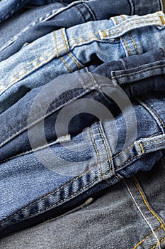Close up of pile of casual black and blue jeans with seam and thread detail. Vertical full frame background