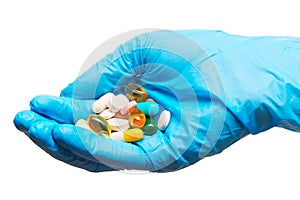 Close up of pile of different tablets and capsules on female doctor's hand in blue sterilized surgical glove