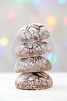 Close up of a pile of four crackled cocoa cookies, arranged like a snowy Christmas tree, against blurred, colorful Christmas