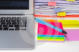 Close-up of a pile of papers with a post-notebook, colored post its and a pen.