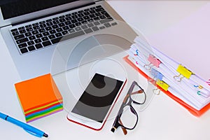 Close-up of a pile of papers with a post-notebook, colored post its and a pen.