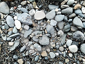 Close up pile of smooth small stones on black sand