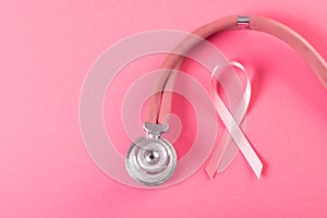 Close-up of pink breast cancer awareness ribbon with stethoscope on pink background, copy space