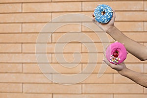 Close-up of a pink doughnut with red cherry and sprinkle glaze and a blue donut with beads held by an american male hand