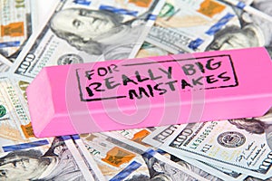 Close up of pink eraser with message for really big mistake on scattered hundred dollar bills