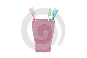 Pink, green and blue toothbrush in plastic cup isolated on white background.