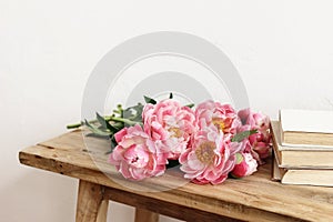 Close-up of pink peonies flowers, bouquet and books. lying on old wooden table. White wall. Selective focus, blurred