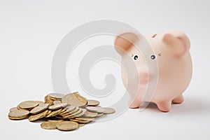 Close up of pink piggy money bank, pile of golden coins on white wall background. Money accumulation