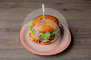 Close-up of pink plate with fresh burger with lettuce, red onion, tomato, chicken punctured with stick on wooden table.
