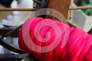 Close up of pink red ball raw merino wool, blurred spinning wheel background