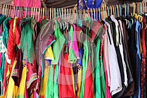 Close-up of pink, red yellow orange, purple, pink, and many designs men and women modern dresses hanging on wood rod in market for