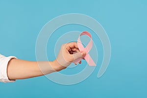 Close up of pink ribbon in hand, symbol of breast cancer awareness, diagnostics and prevention of oncological disease