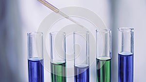 Close up of pipette dropping samples of color liquid into test tubes in laboratory