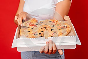Close-up of pizza cut into pieces in a box in female hands isolated on a red background
