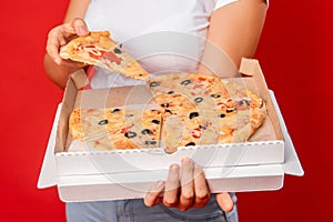 Close-up of pizza cut into pieces in a box in female hands isolated on a red background
