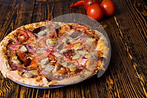 Close up of pizza with ham, tomatoes, sausages and sauce, near a