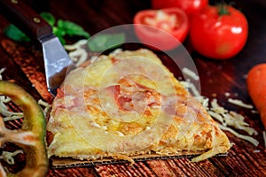 Close-up pizza slice with ham, salami and mozzarella cheese on wooden traditional background surrounded by fresh vegetables