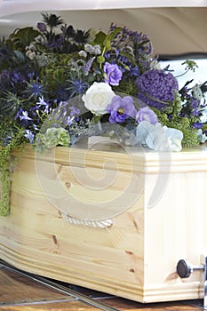 Close Up Of Plain Wooden Coffin With Floral Tributes In Back Of Hearse At Funeral