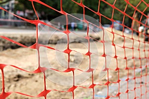 Close-up of plastic orange mesh fencing. Construction or repair of a road to the city