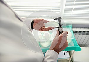 Close-up plastic surgeon hand measuring silicone breast implant size using a calliper. Mammoplasty, Breast augmentation concept.