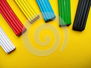 Close-up plasticine of different colors lies on a yellow background with copy space. White, red, yellow, blue, green, black