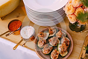 Close-up of a plate with figs and prosciutto on a wooden table with empty clean plates and a bouquet of roses.