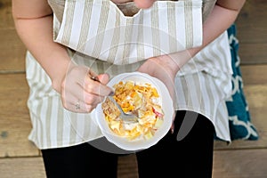 Close-up of plate with fruit salad in hands of eating woman sitting at home
