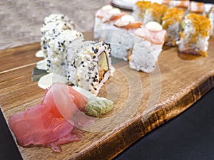 Close up of a plate of Japanese food with different types of uromaki on a wooden board, with a little wasabi and gari in the