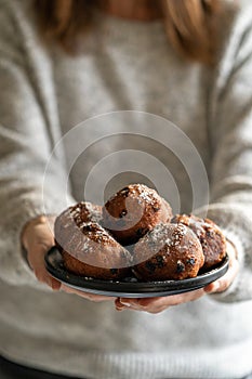 Close-up of a plate of oliebollen (Dutch doughnuts) with icing sugar held by a woman