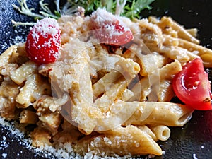 Close-up of a plate with pasta with sauce and parmesan cheese on a black plate in a restaurant