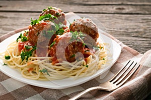 Close up plate of spaghetti with meatballs in tomato sauce sprinkled with parsley on table-napkin on wooden rustic table