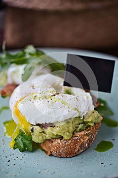 Close-up poached egg with yolk on toast with avocado and salad