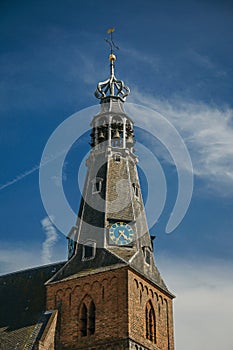 Close-up of pointed steeple roof in a church made of bricks, golden clock and sunny blue sky at Weesp.