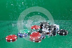 Close up of poker playing chips falling on a green table under the water drops against green background Online gambling.