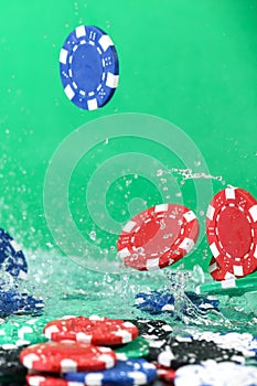 Close up of poker playing chips falling on a green table under the water drops against green background Online gambling.