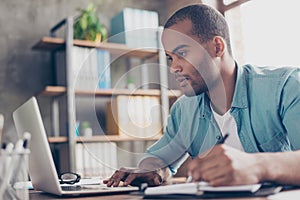 Close up of ponder young african handsome man. He is wearing casual smart, sitting at the workplace, looking in the laptop screen,