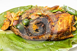 Close-up of popular grilled stingray fish with spices and vegetable served on banana leaf