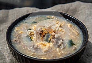 Close-up of Pork congee or Chinese rice porridge with Minced pork, Egg, Enoki mushroom and Seaweed in bowl on white placemat.