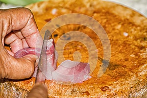 Close up The pork that is placed on the chopping block is being sliced by a knife.